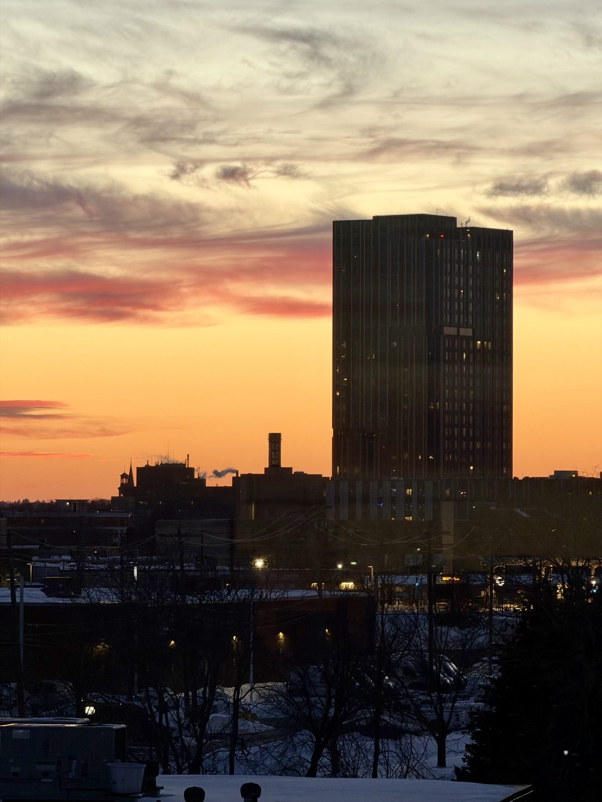 A tower silhouetted against an orange and pink sunset over a snowy Boston skyline