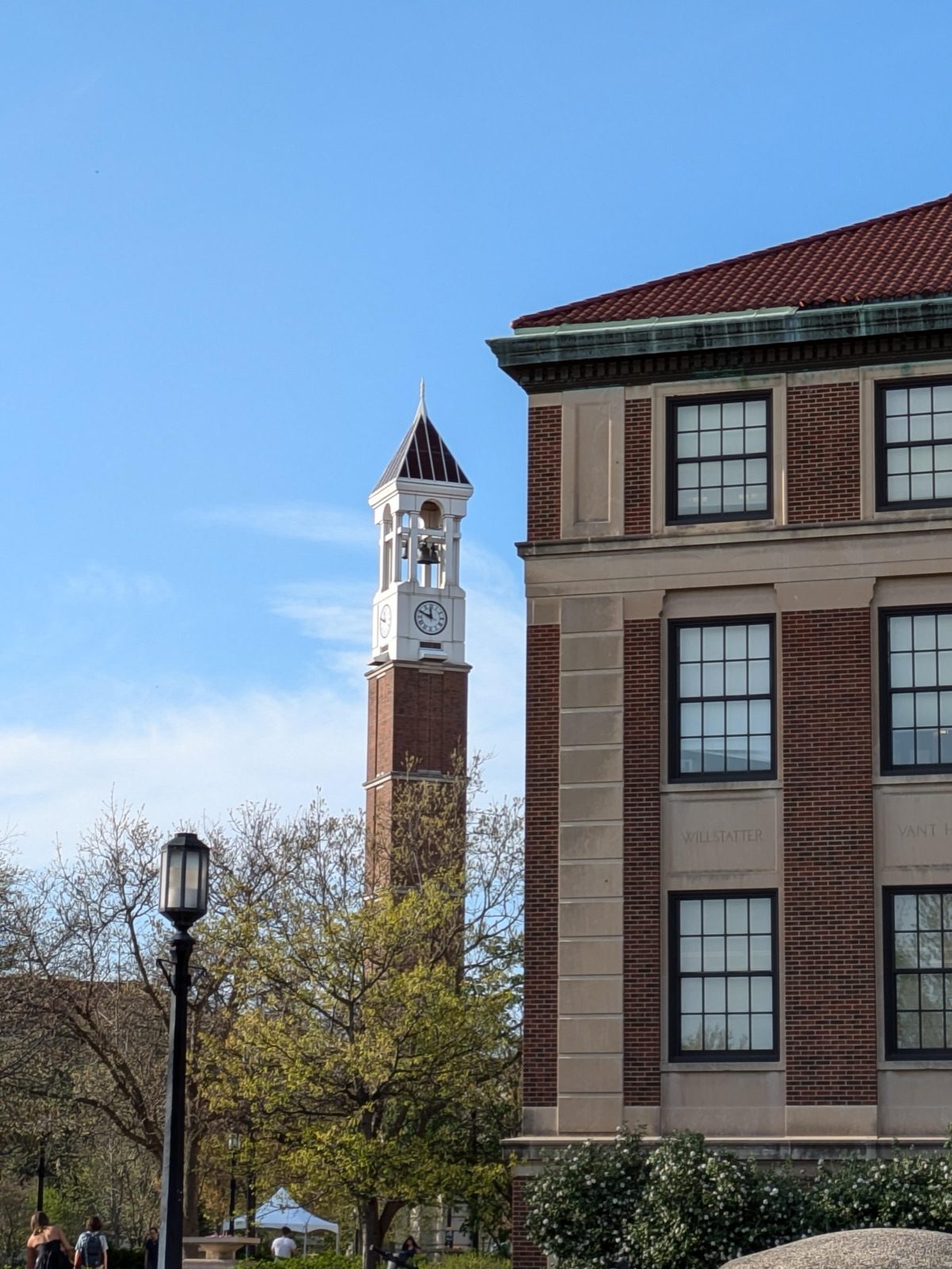 The Purdue bell tower against a clear blue sky, seen past a brick campus building