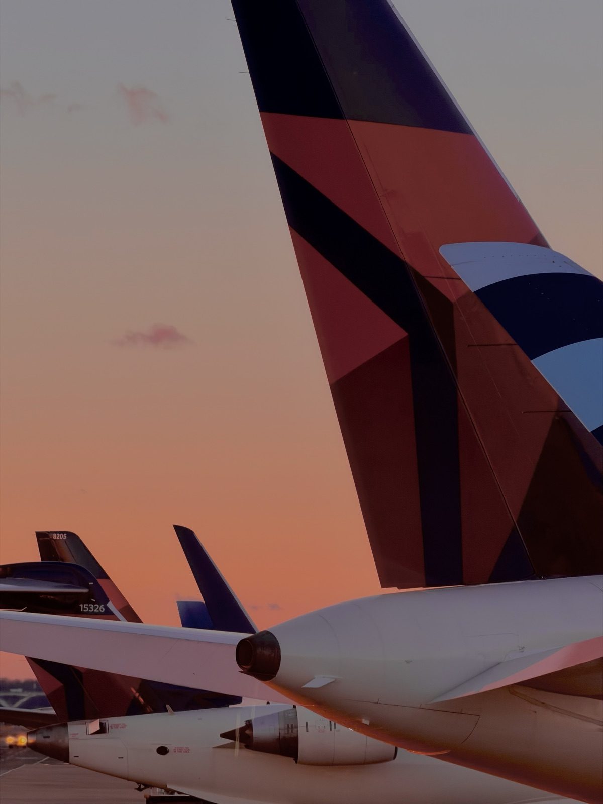 Delta tailfins lined up on the apron at sunset, the sky orange behind them