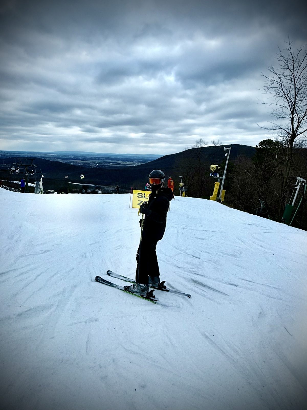 A skier standing at the top of a run under heavy grey cloud, the valley opening out behind